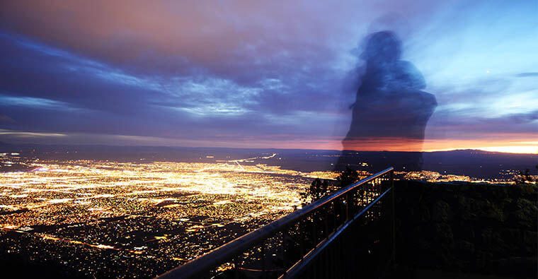 silhouette of a person standing on the Sandia Mountains overlooking city lights at night